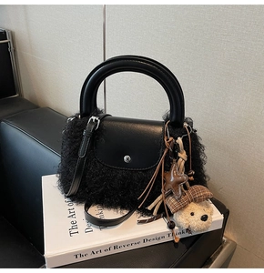 Detalle de bolso de piel sintética negra con correas de cuero y colgante de oso peluche