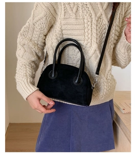 Detail of black matte bowling handbag with leather crossbody strap on a soft knit sweater