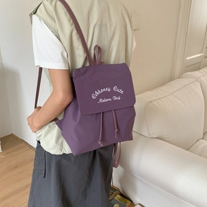Detail view of purple nylon backpack with white embroidery and drawstring side pockets