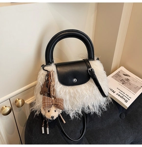 Detalle de bolso de piel sintética blanca con ribete de cuero negro y accesorio de oso peludo