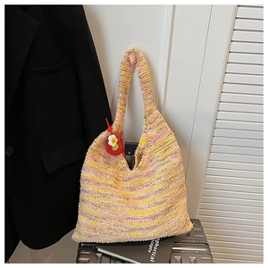 Detailed shot of rainbow woven tote bag with floral charm on a metallic suitcase