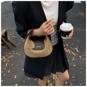 Detail of two-tone half-moon bag featuring suede texture and gold logo on the flap