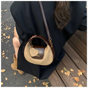Detail of a half-moon leather bag with suede patchwork and heart pendant on a bench
