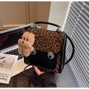 Détail du sac léopard avec rabat noir et breloque ours en peluche sur un bureau