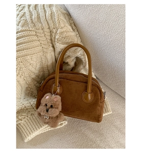 Detail of brown suede tote bag with a cute plush dog charm on cozy knit background