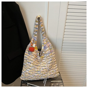 Close-up of a colorful woven rainbow tote bag with an orange fruit pendant on a suitcase