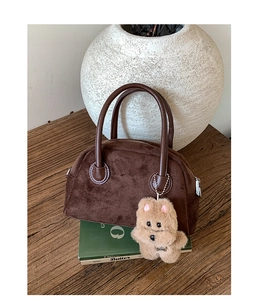 Detail of dark brown suede handbag featuring smooth leather handles and cute bear charm