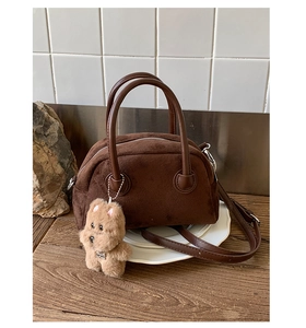 Detail of suede bowling bag with dual handles and a cute plush puppy charm on wood surface