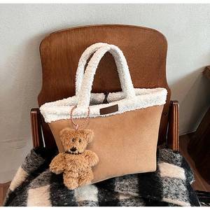 Close-up of suede bucket bag with white faux fur trim and cute brown teddy bear charm
