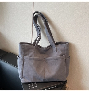 Detail of grey corduroy tote bag with side pockets and retro texture on leather sofa