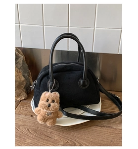 Detail of black suede Boston bag featuring a plush bear charm and leather strap