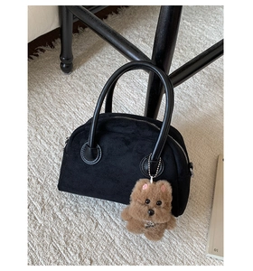 Close-up of black suede Boston bag with leather handles and a plush bear charm