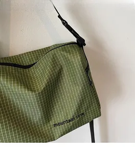 Detail of green checkered shoulder bag with mountain line print and black zipper strap