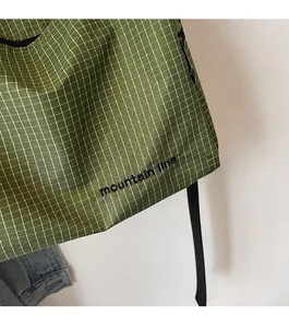 Detail of green plaid canvas bag with mountain line embroidery and woven fabric texture