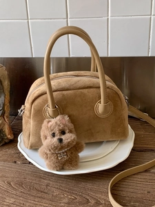 Brown suede Boston bowling bag with leather handles and a plush dog charm on a wooden desk