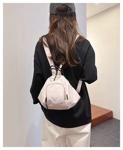Rear view of a light pink mini nylon backpack worn by a model in a modern interior