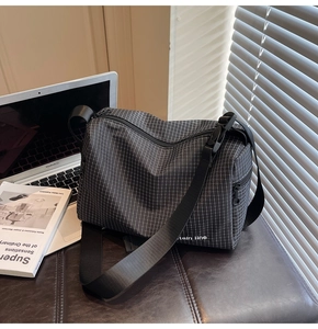 Detail of black and white checkered canvas messenger bag with adjustable strap and zip pocket