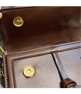 Detail of dark brown glossy leather bag with dual golden magnetic buckles and fine stitching