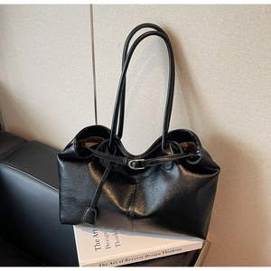 Close-up of minimalist black leather tote bag featuring a sleek silver metal buckle detail