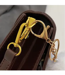 Detailed macro view of the golden metal hook and plush charm on brown leather bag