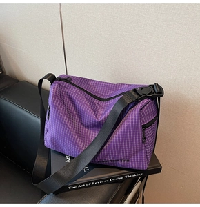 Detail of purple plaid canvas crossbody bag featuring mountain line logo and side zipper