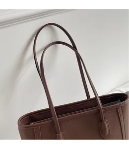 Close-up of dark brown tote bag with pebbled texture and smooth long shoulder straps