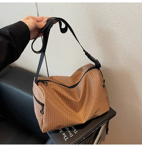Close-up of brown checkered canvas bag with adjustable wide strap and zipper detail