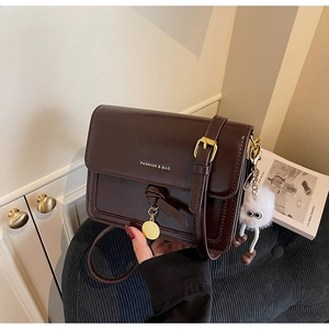 Detail of dark brown glossy leather handbag with gold buckle and plush monster charm