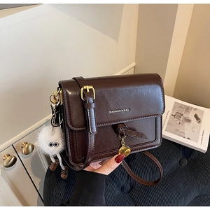 Detailed macro view of retro brown crossbody bag with gold hardware and plush charm