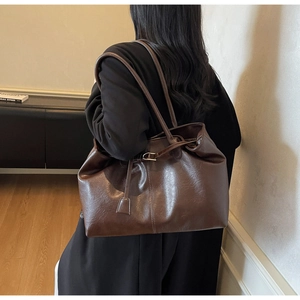 Side view of a large brown leather tote bag with glossy finish on a female model