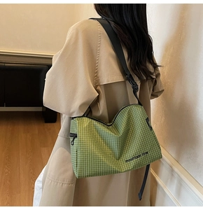 Detail of green checkered messenger bag with black shoulder strap worn by a model