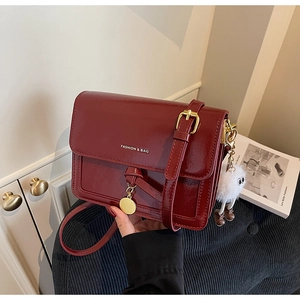 Close-up of wine red leather flap bag featuring gold FASHION & BAG lettering and plush charm