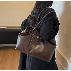 Detail of dark brown matte tote bag featuring side buckle adjustment and fine leather texture
