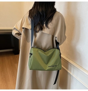 Detail of green plaid canvas crossbody bag featuring adjustable black strap and mountain line text