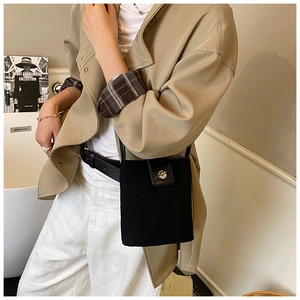 Detail of black mini crossbody bag with silver buckle and leather belt on trench coat