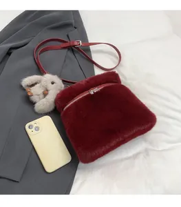 Détail du sac seau en peluche bordeaux avec charm lapin à côté d'un téléphone pour taille