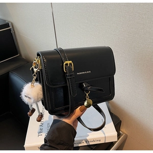 Detail of black glossy leather square bag with white logo and plush monster keychain