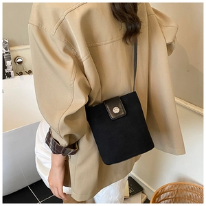 Detail of a black suede bucket bag with leather strap and metal buckle on a model