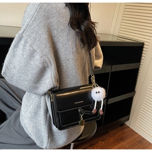 Detail of black vintage square shoulder bag with plush monster charm and golden pendant