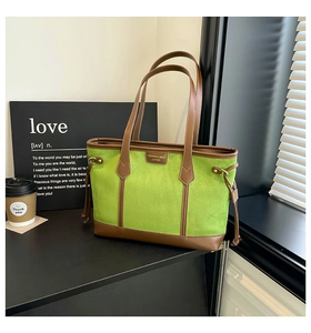 Detail of green tote bag with brown leather trim and side drawstring on dark table