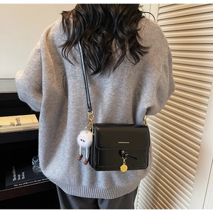 Close-up of black glossy mini flap bag with a quirky white plush monster charm
