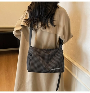 Detail showing the adjustable black nylon strap and zipper on plaid crossbody bag