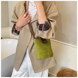 Green suede bucket bag with brown leather strap worn by a model in a stylish outfit