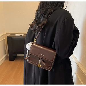 Detail of a deep brown crossbody bag with glossy finish and white fur ball charm accessory