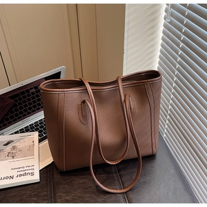 Close-up of brown pebbled leather tote bag in an elegant office setting next to a laptop