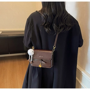 Detail of vintage brown square crossbody bag with plush ball and tassel charm