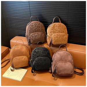 Detail view of mini backpacks in leopard print and solid colors on a leather sofa