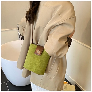 Detail of green suede bucket bag with brown leather flap and round metal buckle close-up