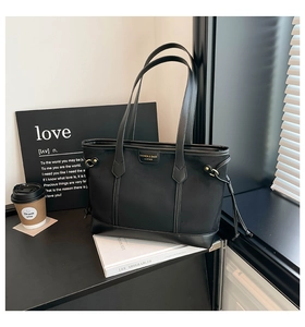 Detail of the high-capacity black tote bag with leather trim and gold metal logo plaque