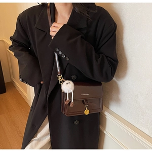Detailed side view of dark brown square crossbody bag with gold charm and plush pendant